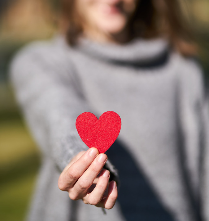 En kvinna räcker fram handen där hon håller i ett rött hjärta.