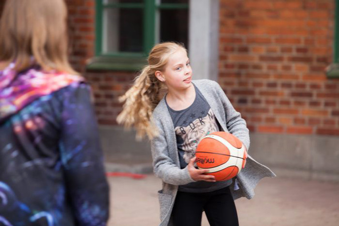 Två barn spelar basket på skolgård.