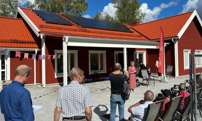 Politiker och boende utanför Åstugans tillbyggnad. Enr röd träbyggnad med solceller på taket.