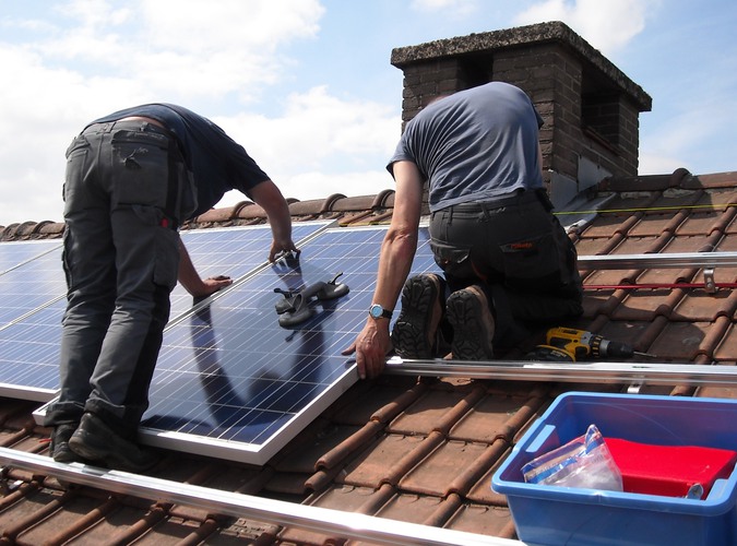 Två personer monterar solceller på ett tak.