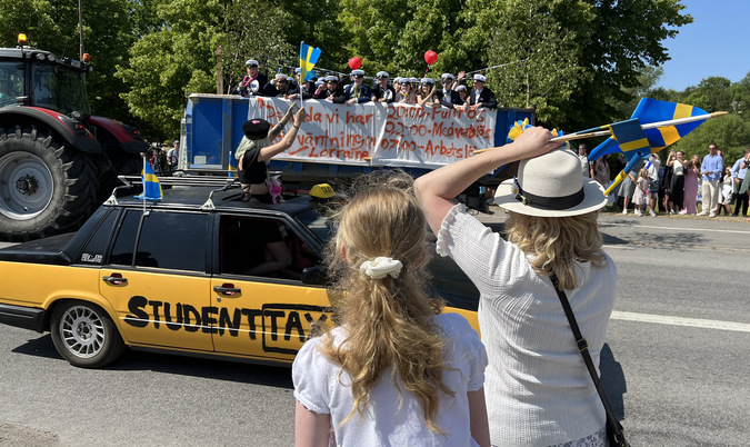 Traktor med flak som studenterna åker på. Det viftas med svenska flaggor.